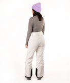 A woman shown from the back wearing a lavender knit beanie, a gray long-sleeve top, and off-white snow pants against a plain white studio background.