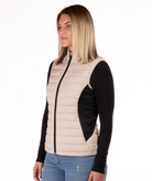 Woman wearing a beige puffer vest over a black long-sleeve shirt on a white background