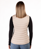 back of a woman wearing a beige puffer vest over a black long-sleeve shirt on a white background