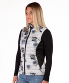 Woman wearing a flower patterned puffer vest over a black long-sleeve shirt on a white background