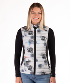 Woman wearing a flower patterned puffer vest over a black long-sleeve shirt on a white background