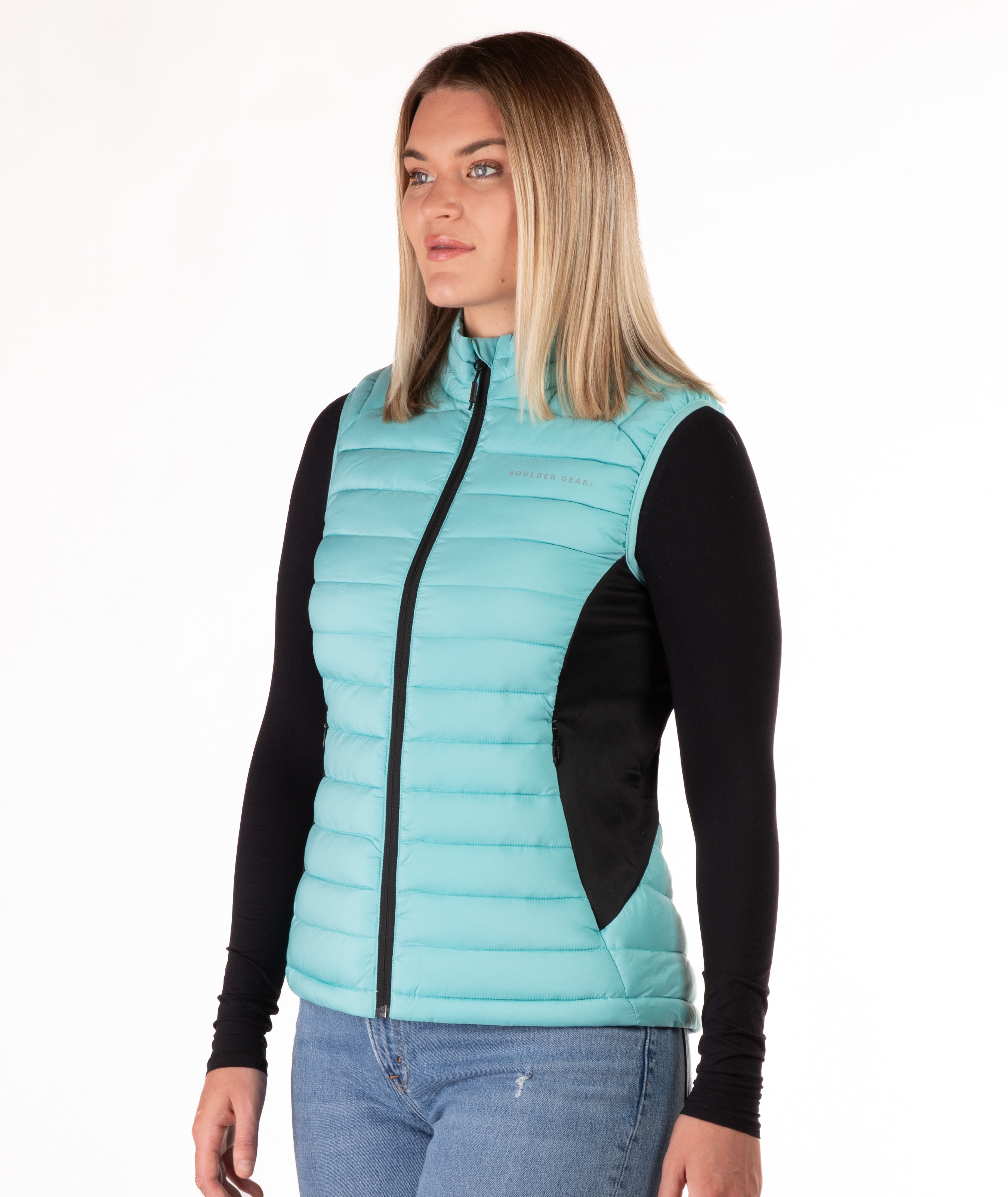 Woman wearing a turquoise puffer vest over a black long-sleeve shirt on a white background