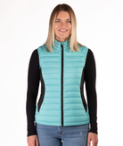 Woman wearing a turquoise puffer vest over a black long-sleeve shirt on a white background