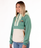 Woman wearing a green and beige fleece pullover with a visible brand logo and orange detailing on a white background