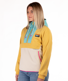 Woman wearing a yellow, blue and beige fleece pullover with a visible brand logo and pink detailing on a white background