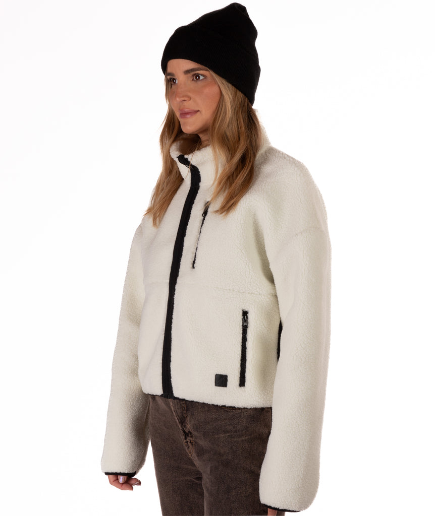 Woman wearing a white fleece jacket with black zipper details on a white background