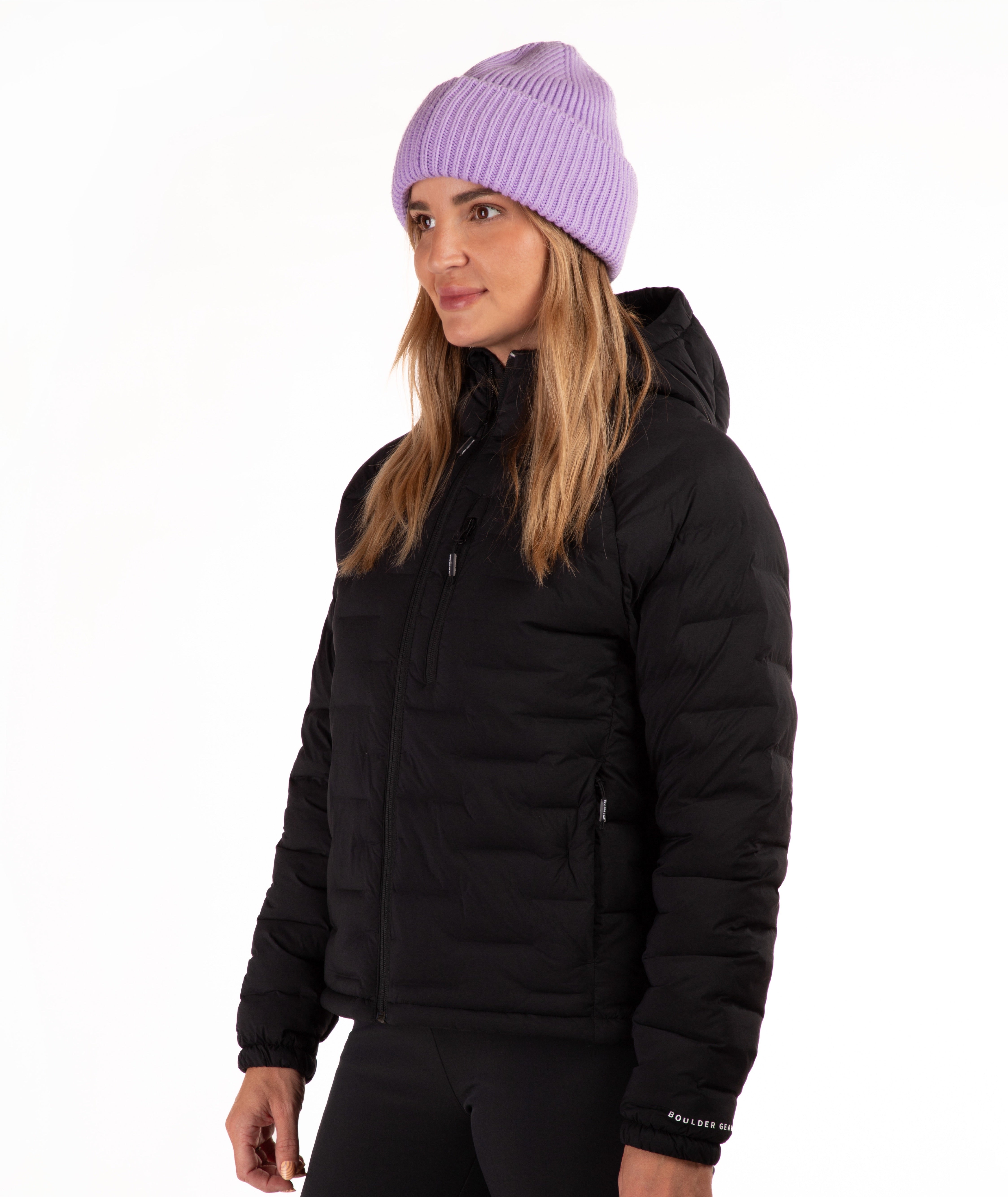A woman wearing a black hooded puffer jacket and a light purple ribbed knit beanie, photographed against a plain white studio background.