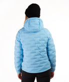 A person shown from the back wearing a light blue hooded puffer jacket, a black beanie, and black pants against a plain white studio background.