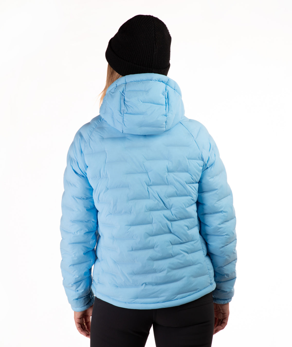 A person shown from the back wearing a light blue hooded puffer jacket, a black beanie, and black pants against a plain white studio background.