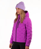 A woman wearing a bright purple quilted hooded puffer jacket and a matching purple ribbed knit beanie, shown in profile against a plain white background.