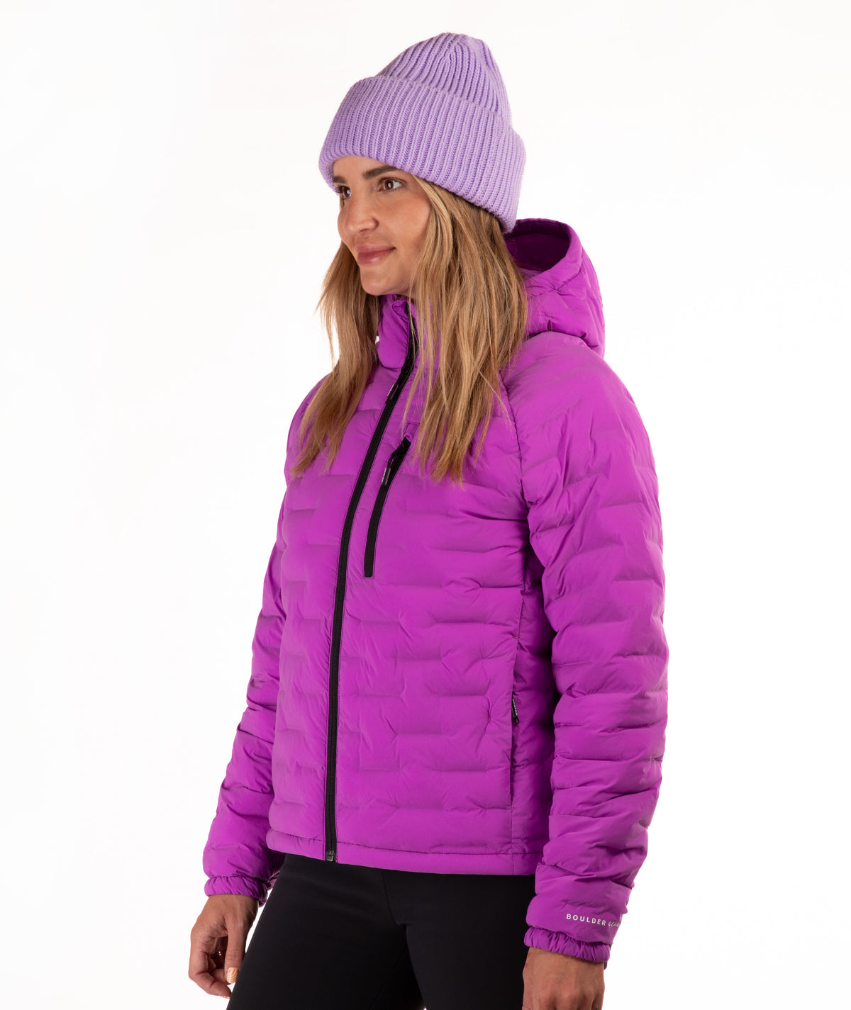 A woman wearing a bright purple quilted hooded puffer jacket and a matching purple ribbed knit beanie, shown in profile against a plain white background.