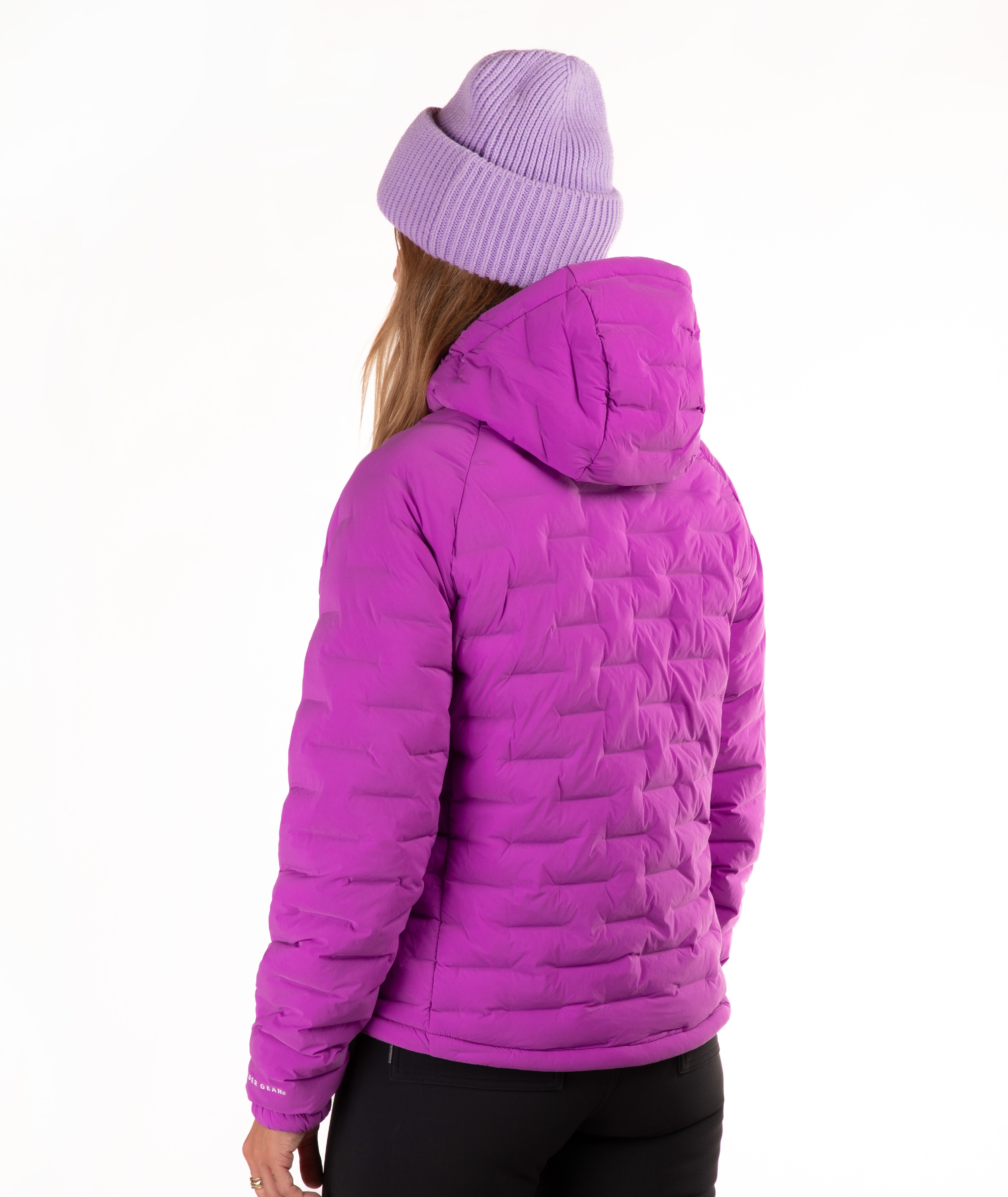 A person shown from the back wearing a bright purple quilted hooded jacket, a light purple ribbed beanie, and black pants against a plain white studio background.