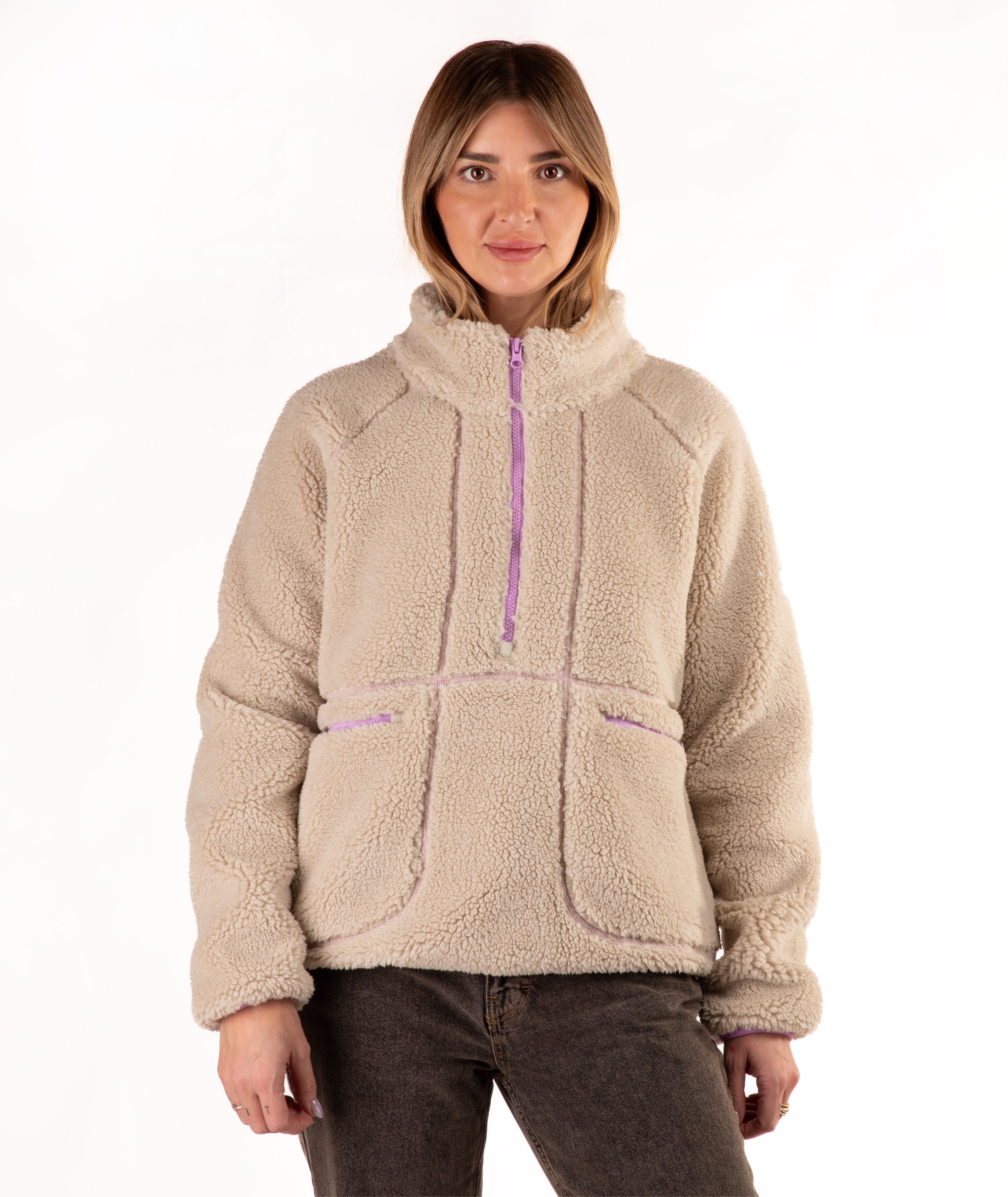 A woman wearing a beige sherpa fleece pullover jacket with a purple zipper and trim, paired with dark brown pants, against a plain white background.