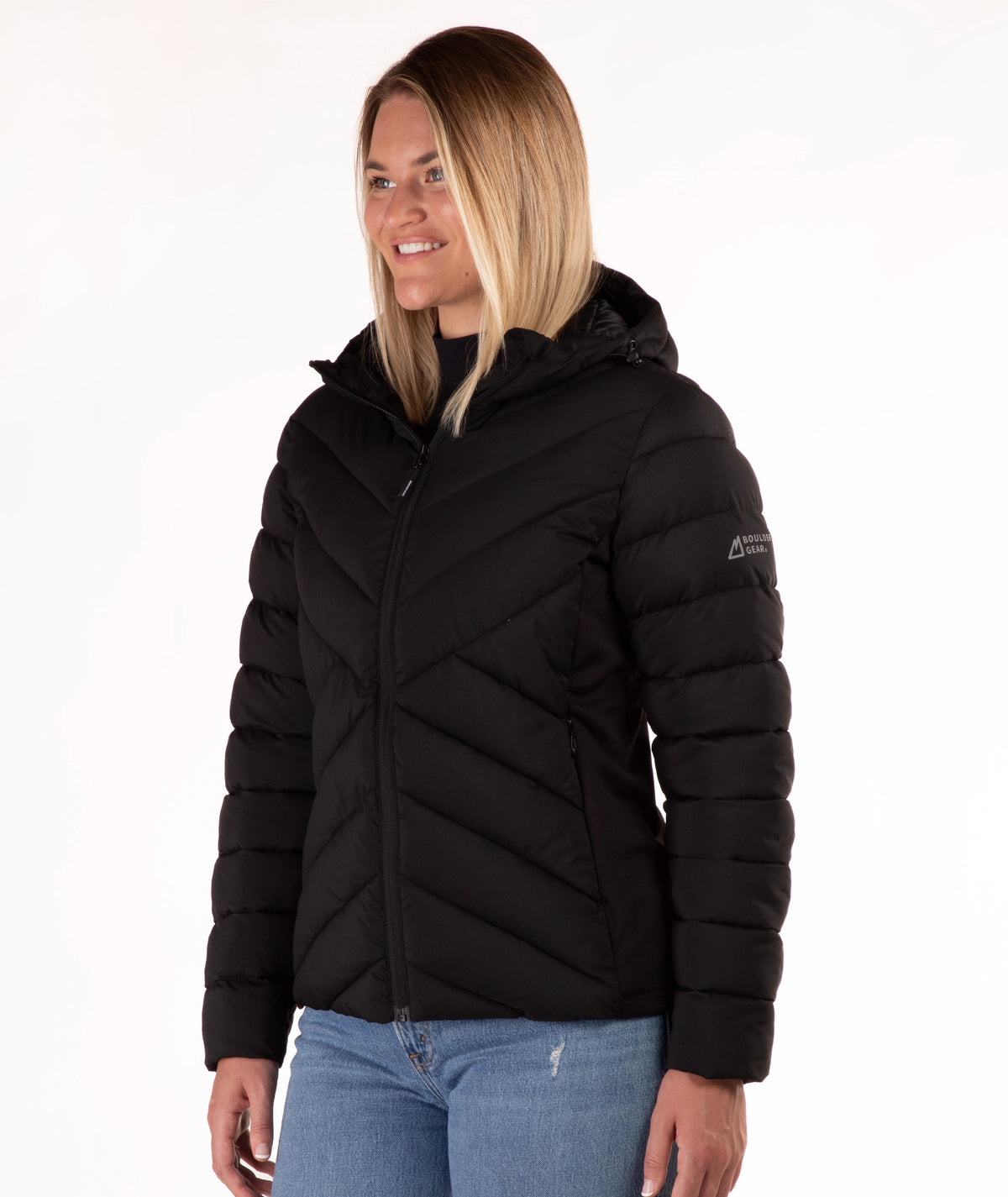 A woman wearing a black hooded puffer jacket paired with blue jeans, photographed against a plain white studio background.