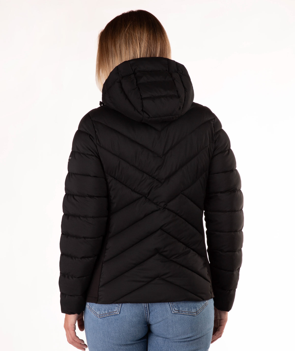 A woman viewed from the back wearing a black hooded puffer jacket with a distinctive chevron quilted pattern, paired with blue jeans, against a plain white background.