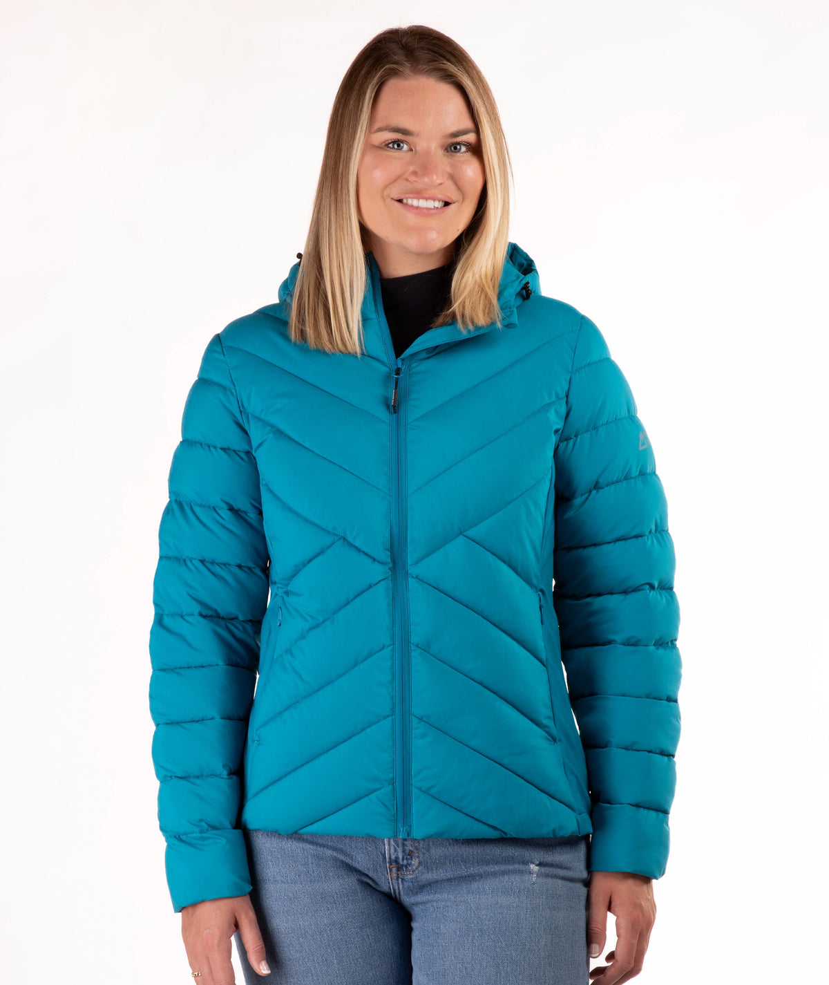 A woman wearing a teal quilted puffer jacket with a hood and front zipper, paired with blue jeans, photographed against a plain white studio background.