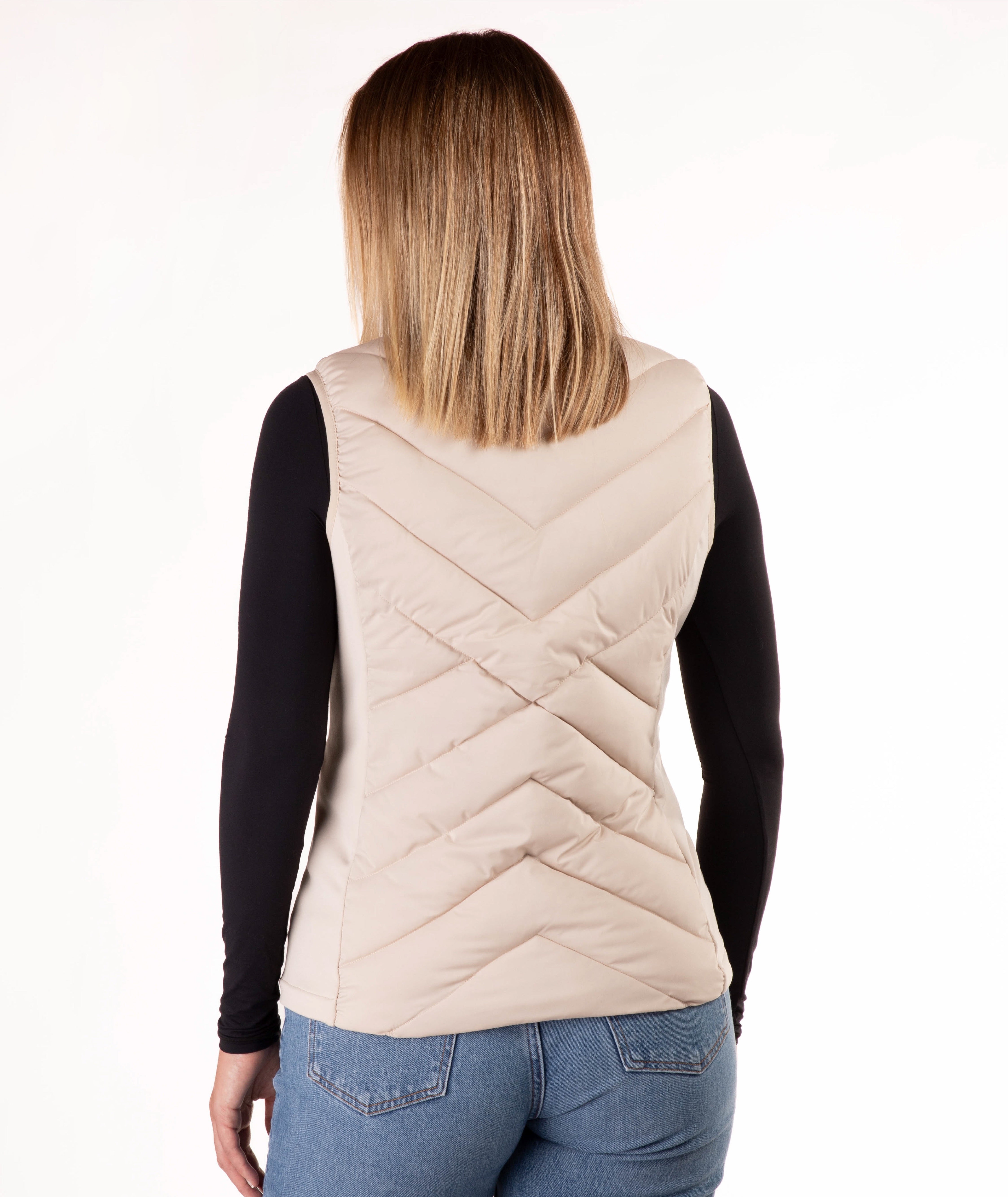 A woman viewed from the back wearing a light beige quilted puffer vest over a black long-sleeve top and blue jeans, against a plain white background.