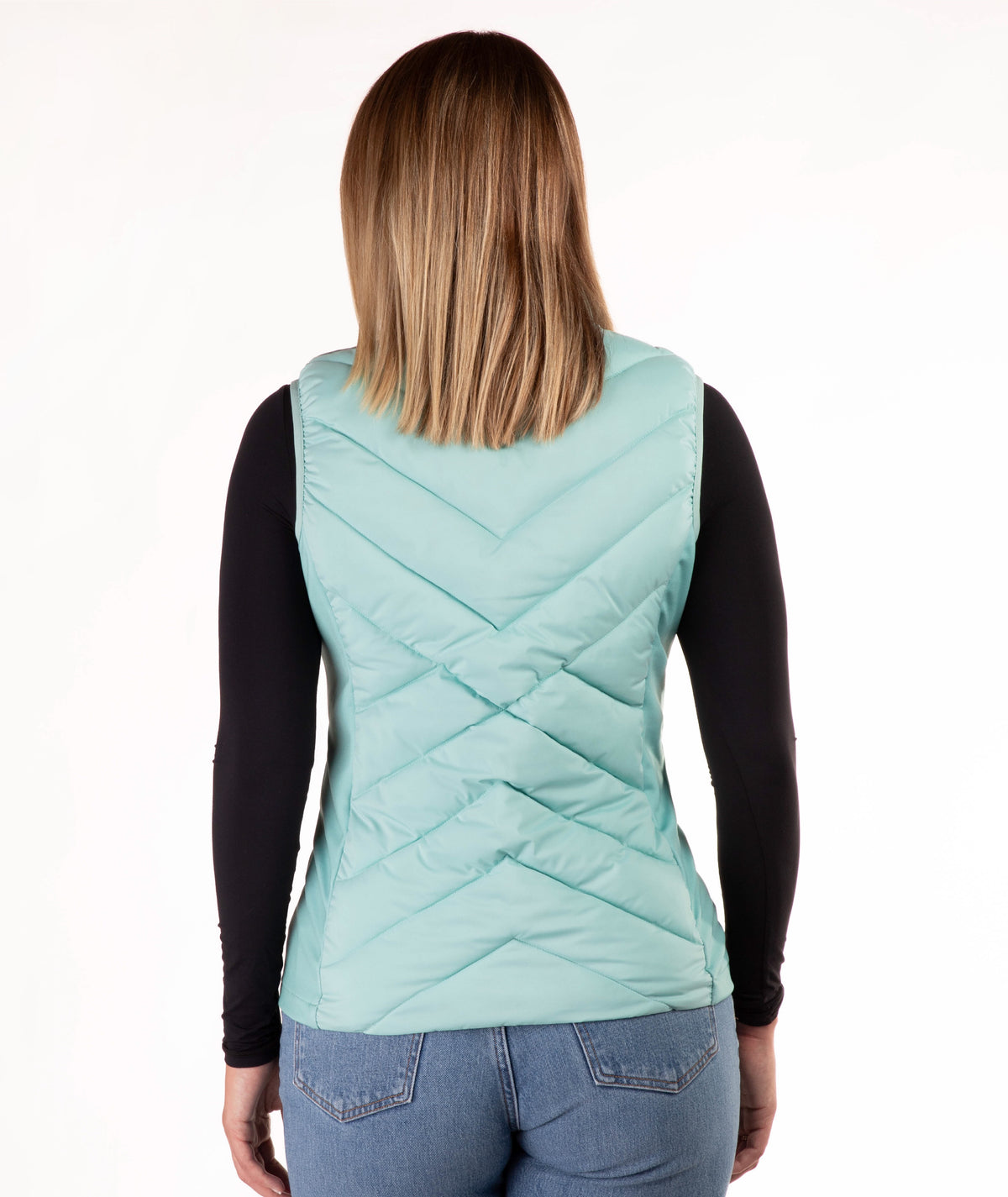 A woman viewed from the back wearing a mint green quilted puffer vest over a black long-sleeve shirt and blue jeans, against a plain white background.