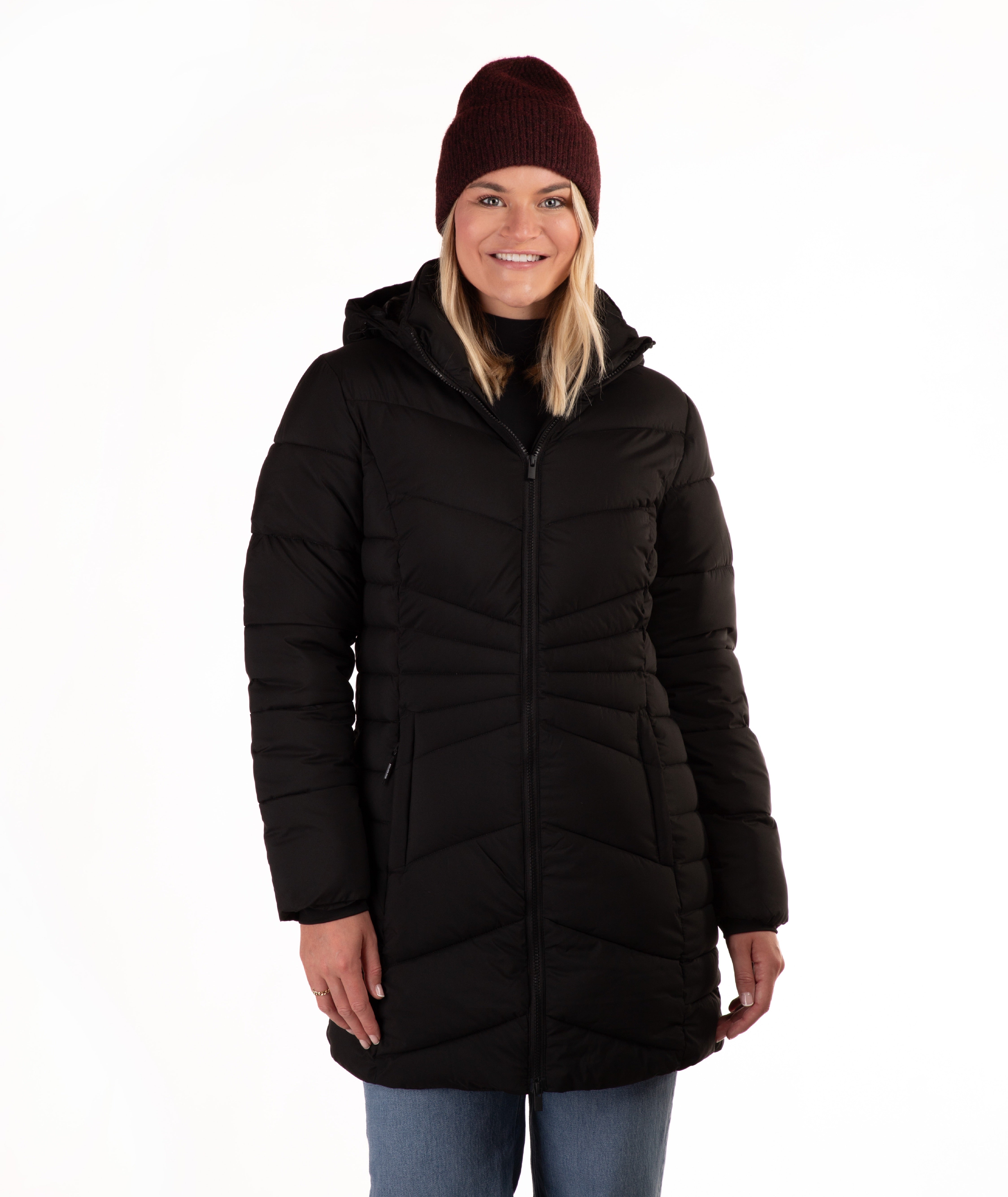 A woman wearing a black hooded puffer coat, a dark burgundy knit beanie, and blue jeans, standing against a plain white background.