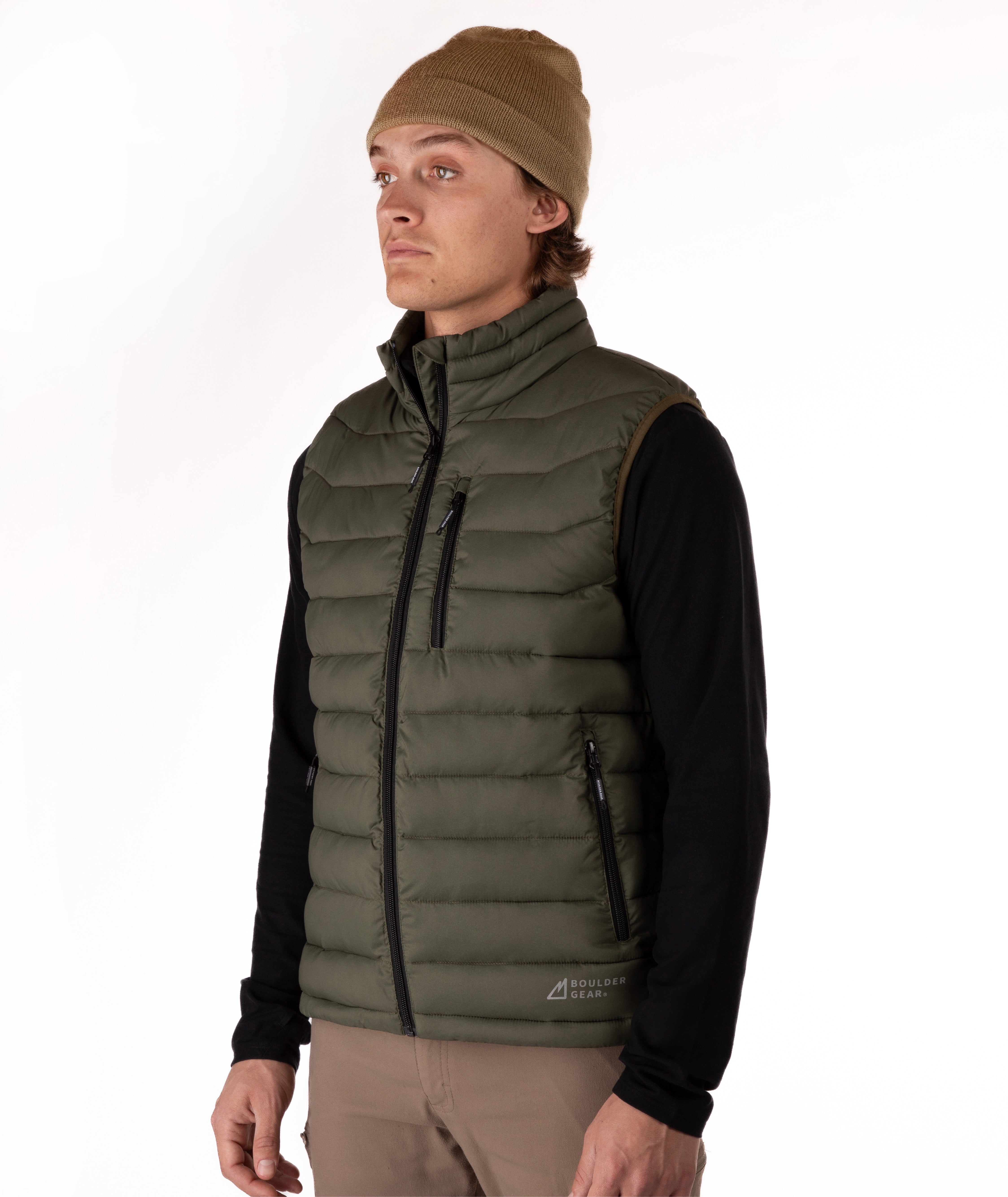 A man wearing an olive green puffer vest over a black long-sleeve shirt, with a brown beanie and tan pants, standing against a plain white background.