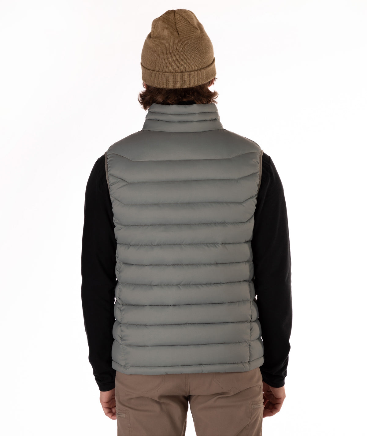A person shown from the back wearing a taupe quilted puffer vest over a black long-sleeve shirt, with a tan beanie and tan pants, against a plain white studio background.