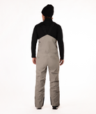 back of Person wearing a black long-sleeve shirt and beige bib overalls on a white background