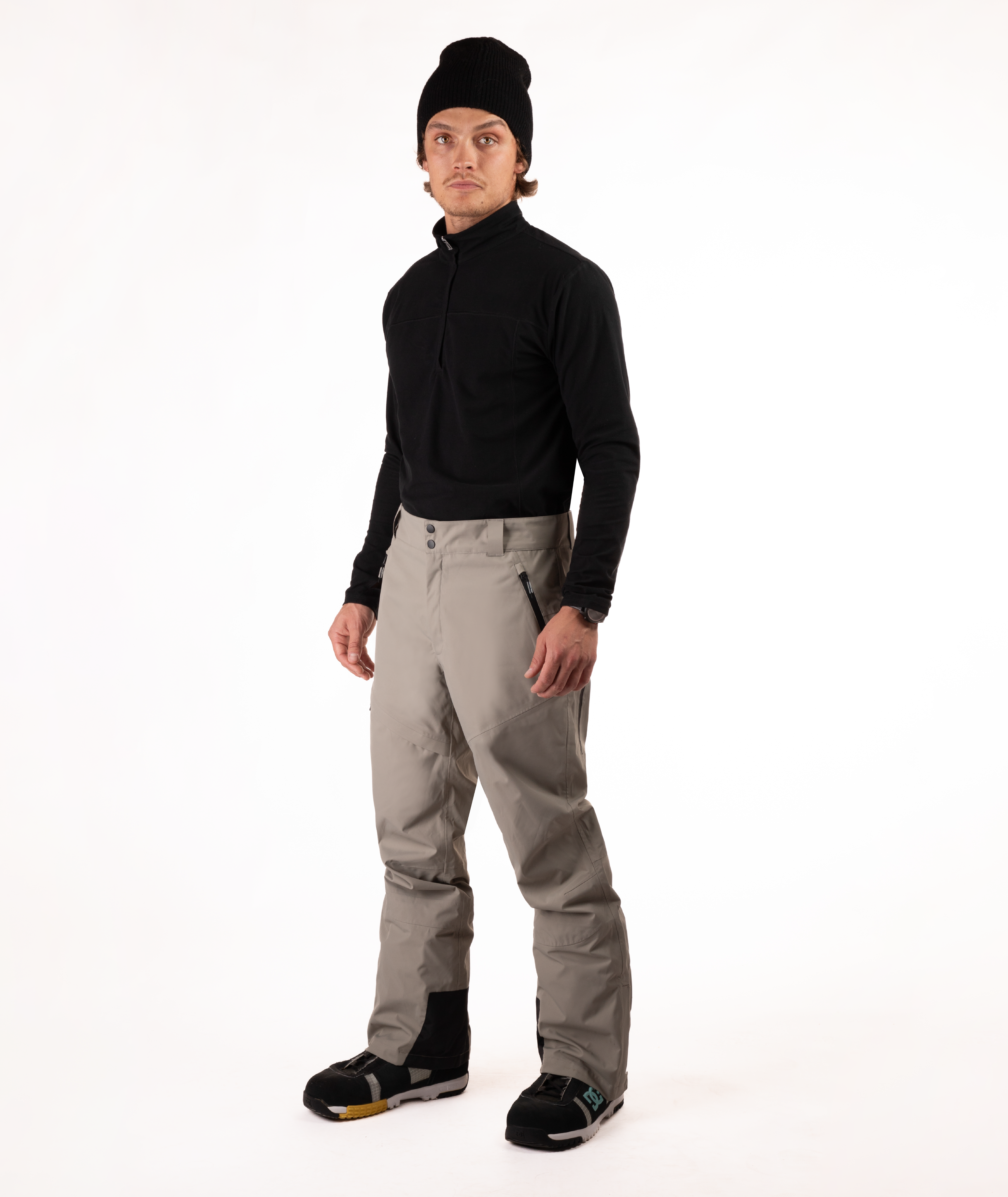 Person wearing a black top and beige snow pants on a white background