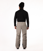 back of a person wearing a black top and beige snow pants on a white background