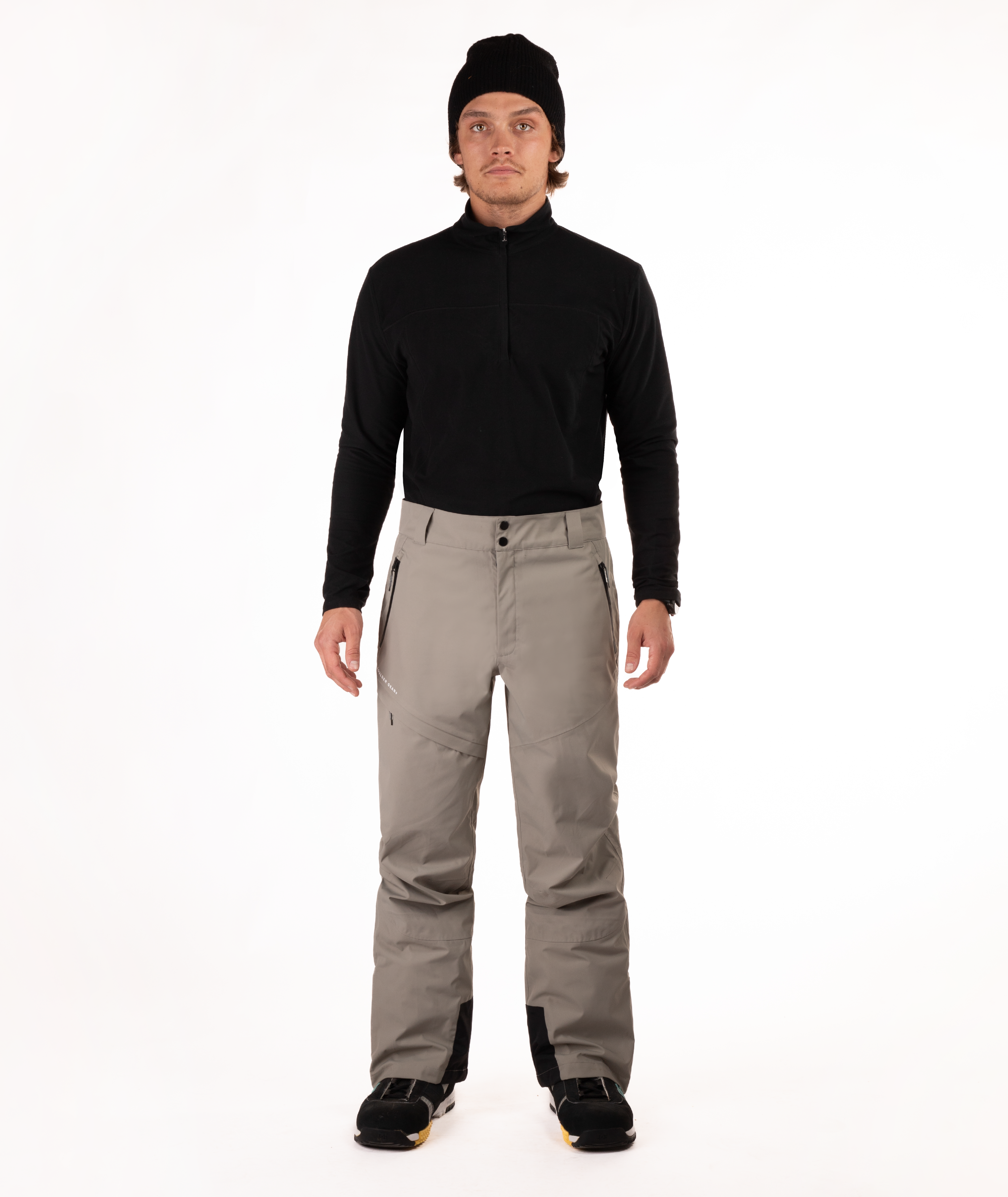 Person wearing a black top and beige snow pants on a white background