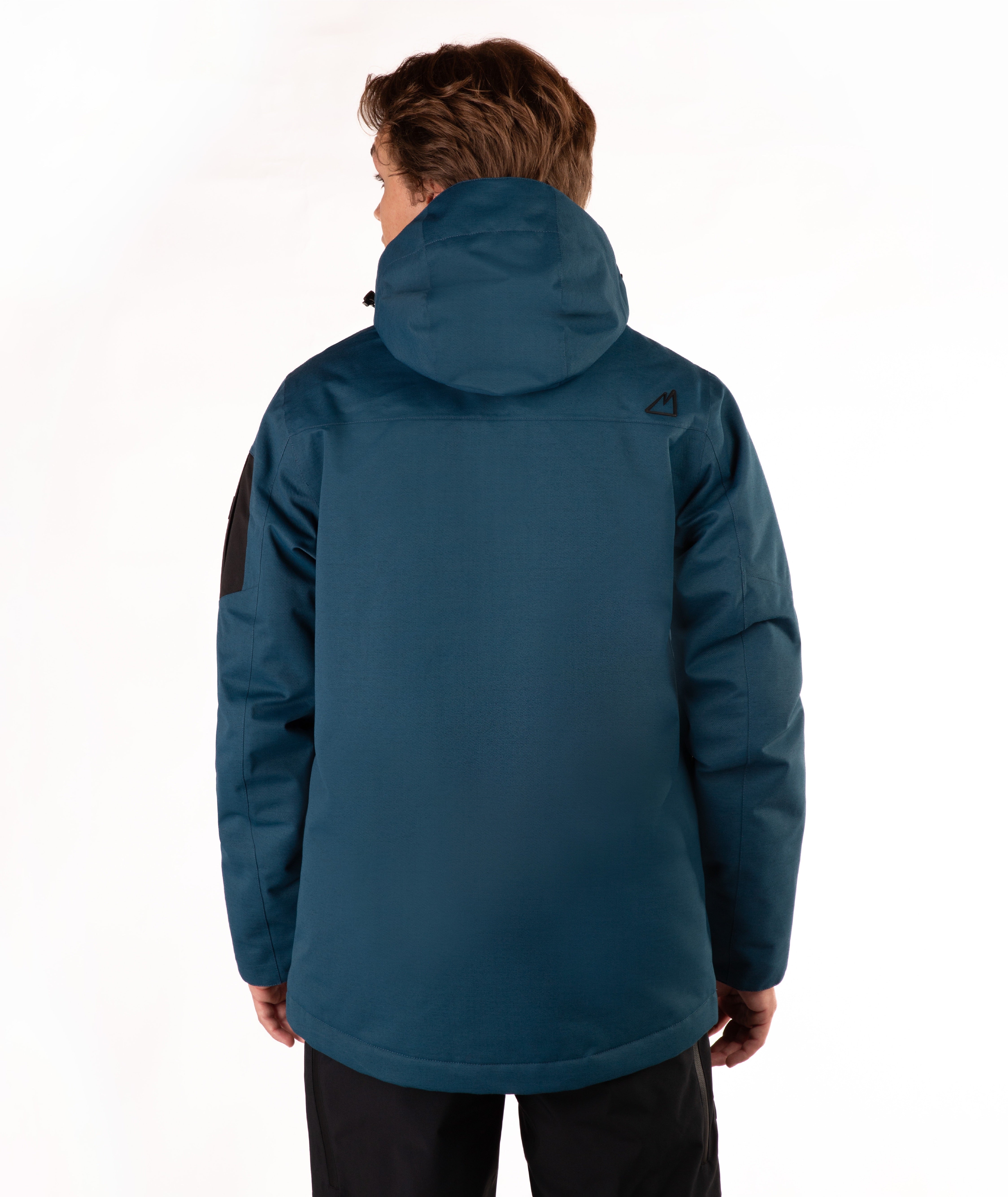 A man viewed from the back wearing a dark teal hooded jacket with a small black geometric logo on the upper right shoulder, set against a plain white studio background.