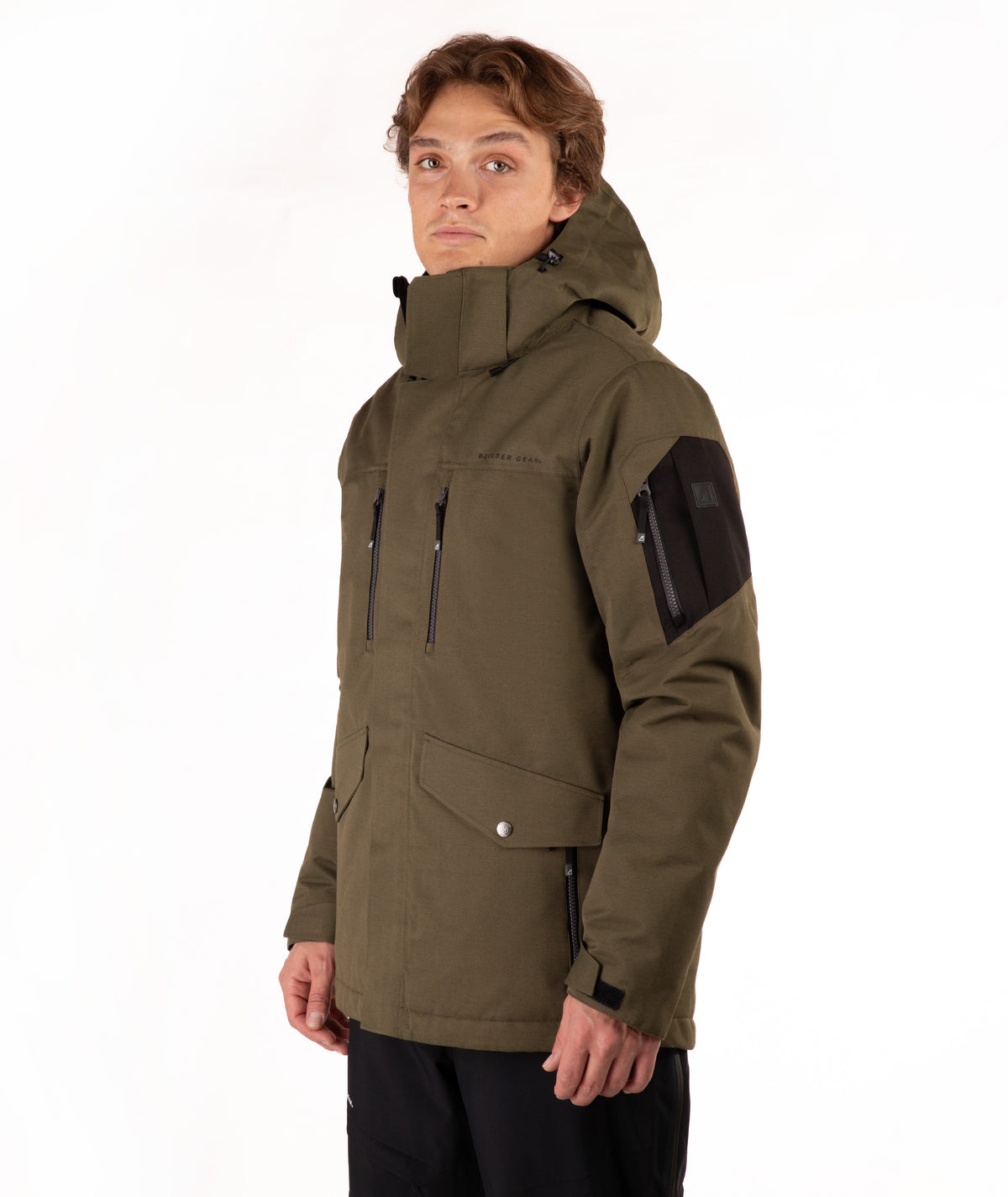 A man wearing an olive green hooded technical jacket with black accents, including a black sleeve patch and black pants, photographed against a clean white studio background.
