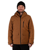 A man wearing a brown hooded technical jacket with black zippers, a black beanie, and black pants, photographed against a plain white studio background.