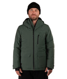 A man wearing a dark green hooded snowboard jacket with black zippers and a black beanie, photographed against a solid white background.