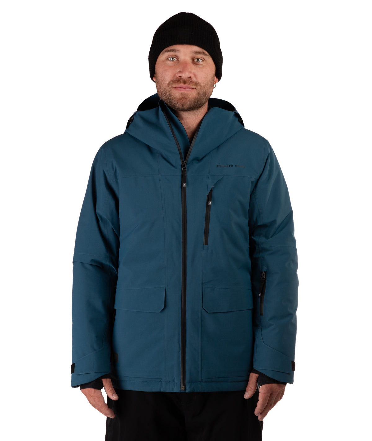 A man wearing a dark teal hooded winter jacket with black zippers, a black beanie, and black pants, photographed against a plain white studio background.