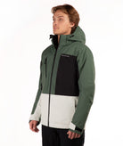 A man wearing a color-blocked ski jacket in dark green, black, and light green against a plain white background.
