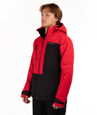 A man wearing a red and black color-blocked ski jacket with a full-zip front and hood, standing against a plain white studio background.
