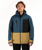A man wearing a color-blocked outdoor jacket, featuring teal blue, black, and mustard yellow sections, photographed against a plain white studio background.