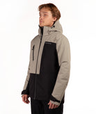 A man wearing a color-blocked ski jacket in beige and black, featuring a full-zip front, a vertical zip pocket on the chest, shot against a plain white background.