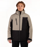 A man wearing a color-blocked ski jacket in beige and black, featuring a full-zip front, a vertical zip pocket on the chest, shot against a plain white background.