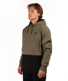 A man wearing a color-blocked pullover hoodie with an olive green upper section and a black lower section, standing against a plain white background.