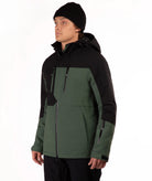 A man wearing a black and dark green color-blocked ski jacket, a black beanie, and black pants, standing against a plain white studio background.