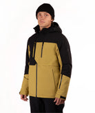 A man wearing a color-blocked ski jacket in black and mustard yellow, paired with a black beanie, photographed against a plain white studio background.