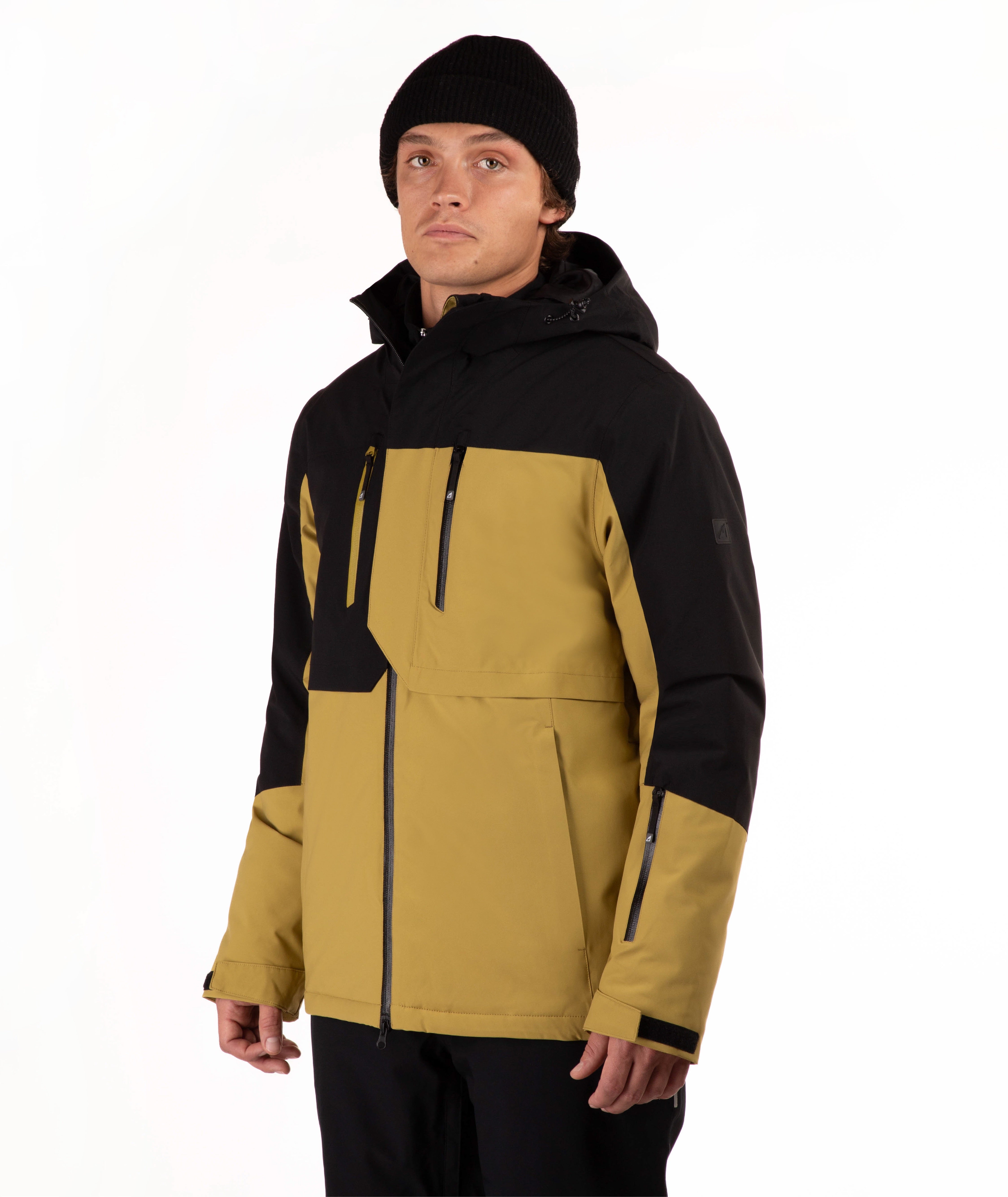 A man wearing a color-blocked ski jacket in black and mustard yellow, paired with a black beanie, photographed against a plain white studio background.