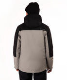 A person shown from the back wearing a two-tone outdoor jacket with a black hood and black sleeves, paired with a taupe body panel, black pants, and a black beanie against a plain white background.