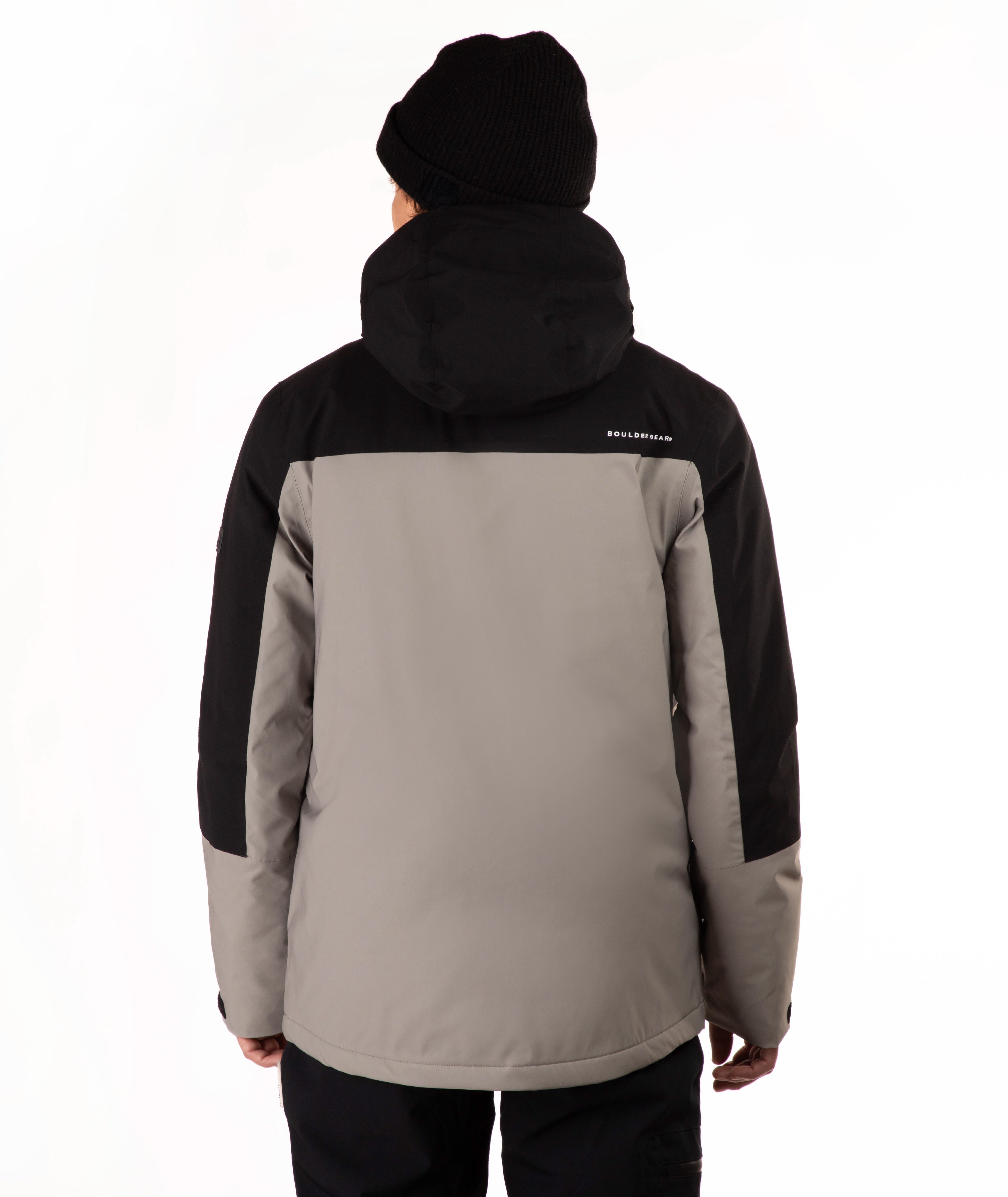 A person shown from the back wearing a two-tone outdoor jacket with a black hood and black sleeves, paired with a taupe body panel, black pants, and a black beanie against a plain white background.
