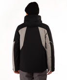 A person shown from the back wearing a black and gray hooded jacket, a black beanie, and gray pants against a plain white studio background.