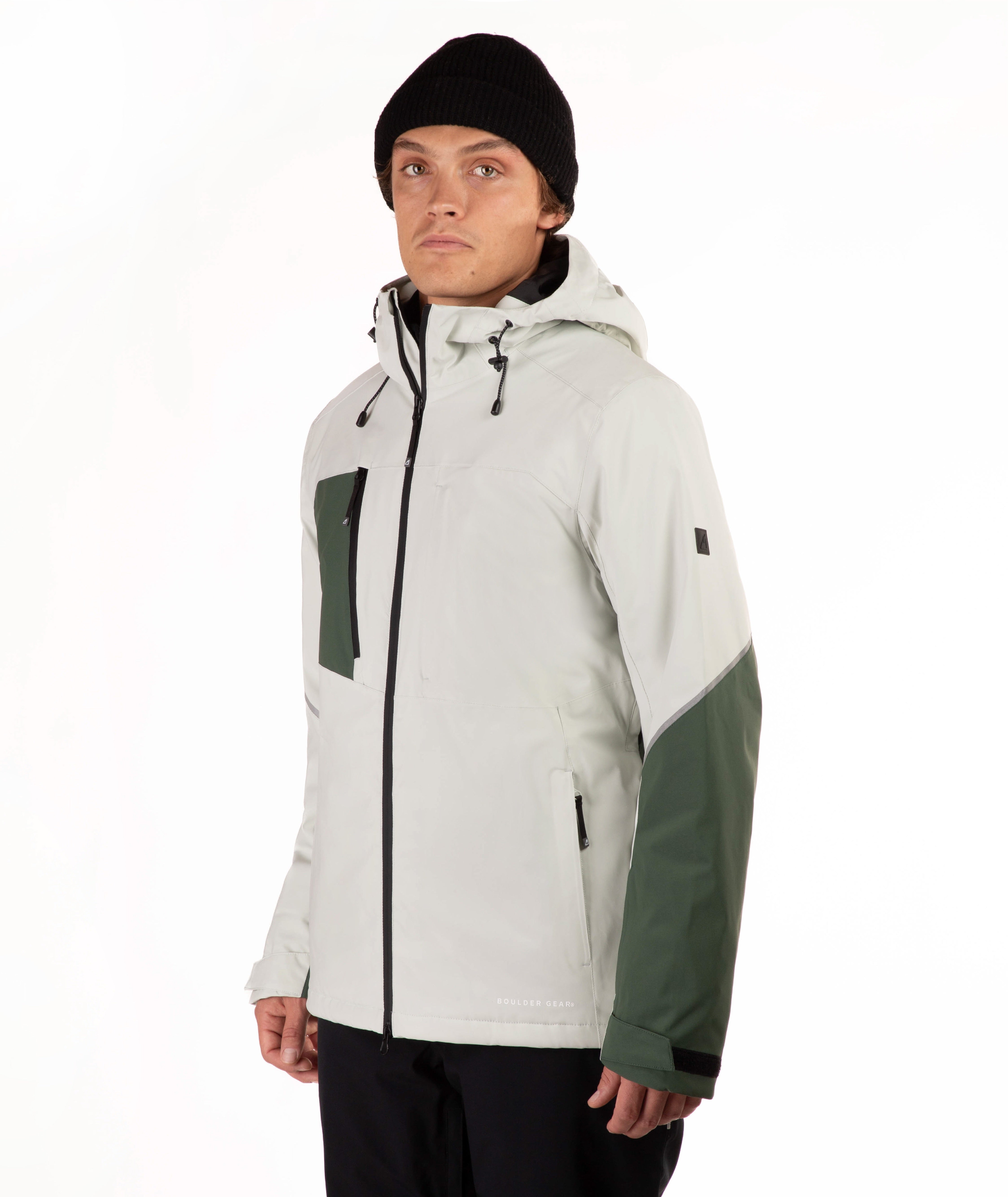 A man wearing a light green and dark green color-blocked outdoor jacket, a black beanie, and black pants, standing against a plain white studio background.