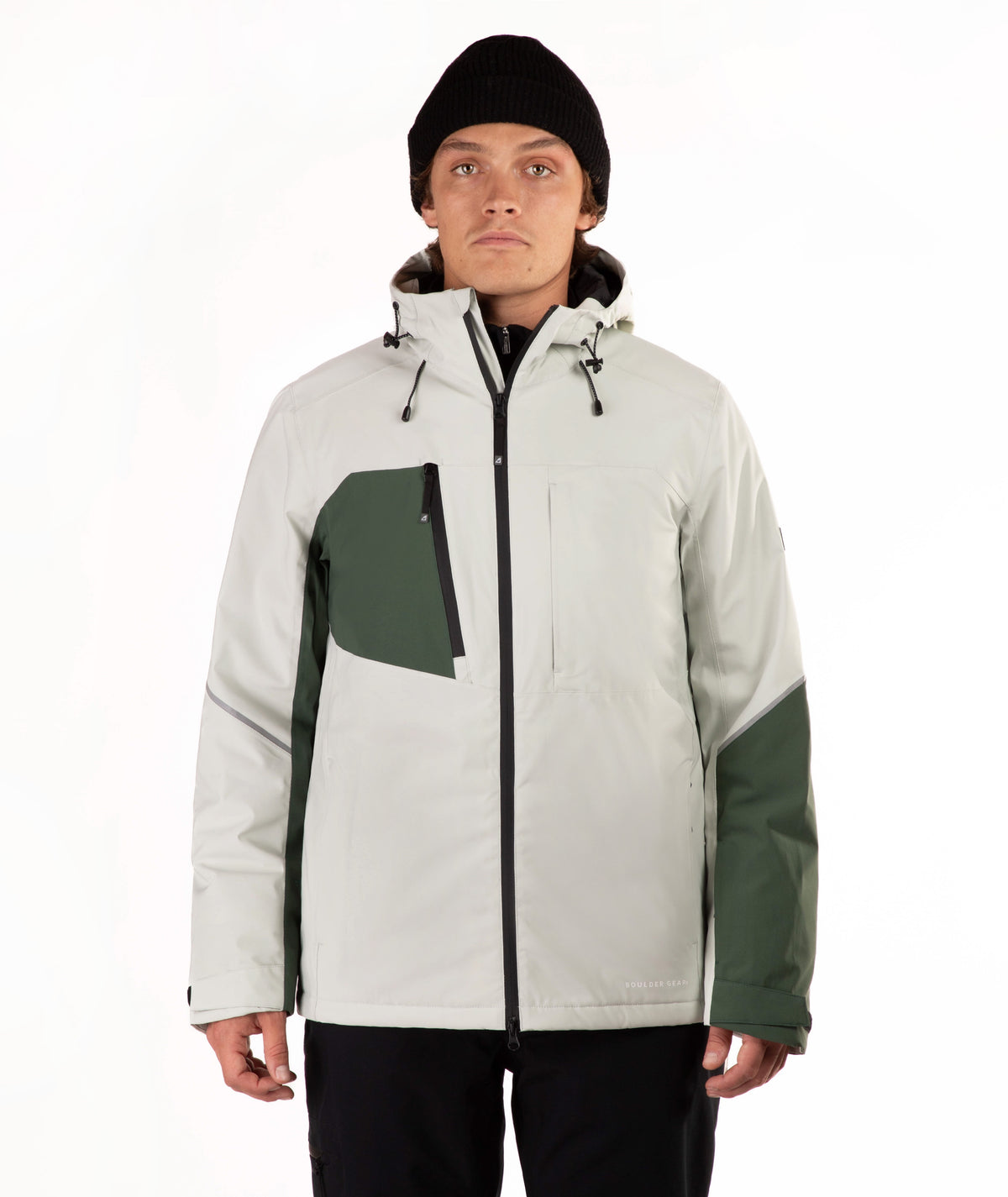 A man wearing a light green and dark green color-blocked outdoor jacket, a black beanie, and black pants, standing against a plain white studio background.