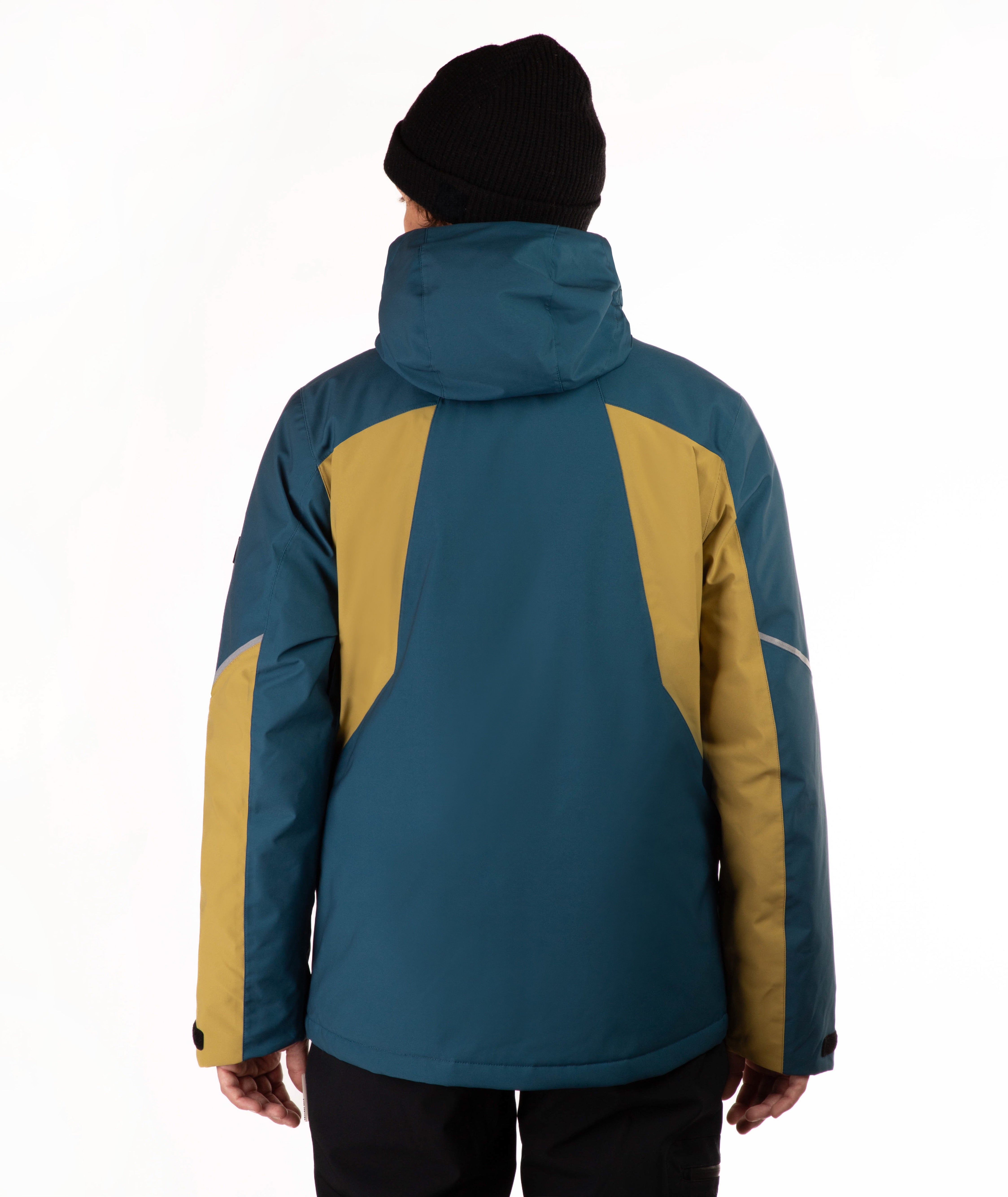 A person viewed from the back wearing a colorblock hooded jacket in teal and mustard yellow, paired with a black beanie and dark pants, against a plain white studio background.