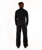 A man viewed from the back wearing a black long-sleeve top and black pants against a plain white studio background.